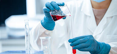 Gloved hands pouring red liquid in to tube